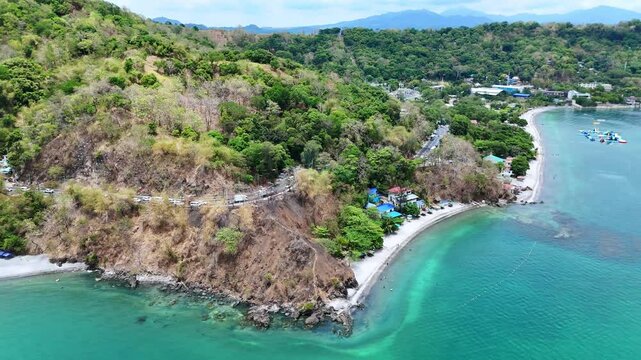 Aerial 4K morning drone footage of Mabayuan Beach in Olongapo, Zambales, Philippines, showing turquoise waves lapping white sand with rugged mountains and a distant city skyline.