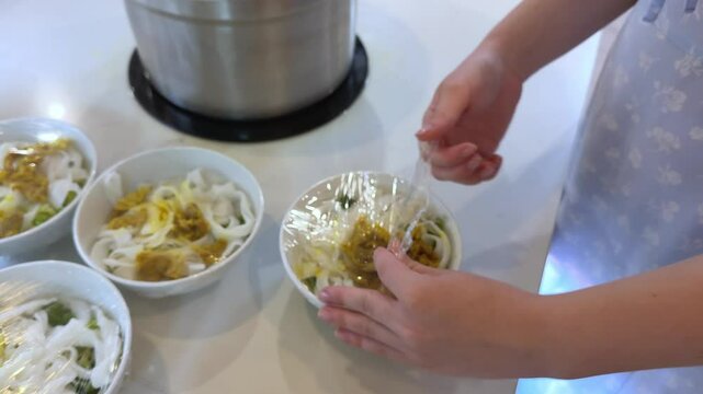 Pouring hot meatballs into a bowl with a plastic wrap base using a round spoon from a hot pot at a meatball vendor's cart. Meatballs are a popular food in Indonesia
