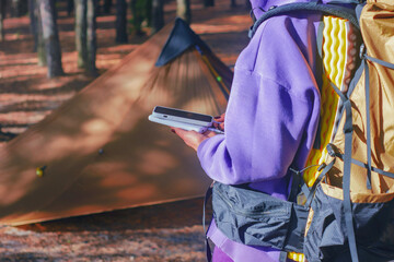 Close-up a woman with a hiking backpack and a smartphone and portable power bank in hands, against...