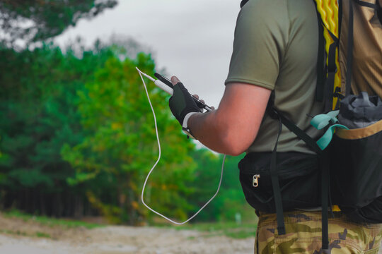 Close-up of a male hiker wearing a green shirt and backpack, charging his smartphone with a portable power bank during an outdoor adventure.