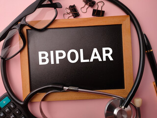 Wooden board and doctor's equipment with the word BIPOLAR on a pink background