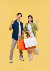 Happy shoppers showcasing shopping bags and gesturing in a bright cheerful yellow studio shot