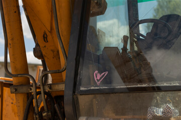 A detailed closeup of a bulldozer cab presents a heart sticker prominently displayed on the window,...