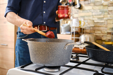 A person adding a rich tomato paste to a pot in a kitchen setting