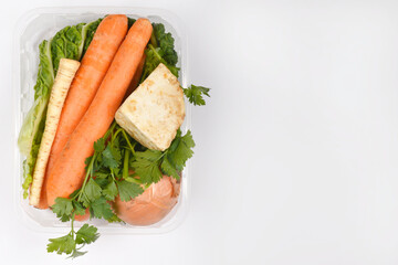 fresh soup vegetables, including carrots, parsley, celery, onion, and parsnip, packaged in a clear plastic container