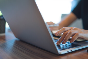 Close up of business woman online working on laptop computer with notebook on table at coffee shop. Student studying online class, taking note on notepad, e-learning, business planning