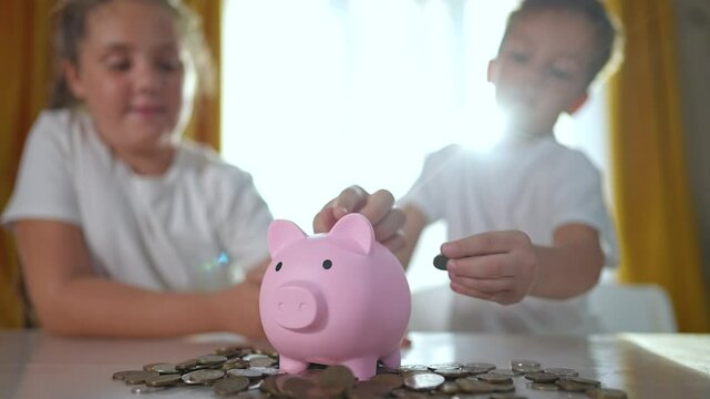 Children saving money piggybank. Children putting coin into pink piggybank at table. Teaching children about money saving with piggybank. kids learning financial habits by filling piggybank at table.