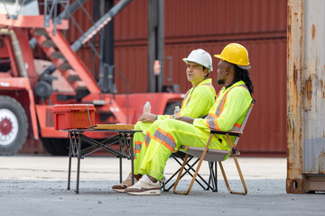 Two Construction Workers on Break at Industrial Site, Diverse Male Laborers Resting Outdoors with Safety Gear, Workers Taking a Lunch Break at Industrial Port