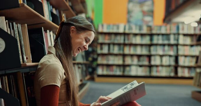 Happy woman, laughing or reading with story in library for comedy, funny joke or humor. Female person, student or learner with smile, book or novel on floor for comic, genre or amusement by bookshelf