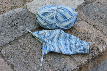 hellblau gemusterte Sockenwolle mit halb gestricktem Socken, Stricknadeln im Strickgut, liegen auf...