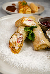 Close-up of pancake rolls with cottage cheese filling sprinkled with powdered sugar. Nutritious breakfast or dessert. Cooking and baking.