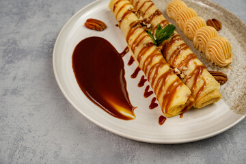 Plate with pancake rolls with chocolate glaze and nut paste on a gray background. Dessert. Cooking and baking.