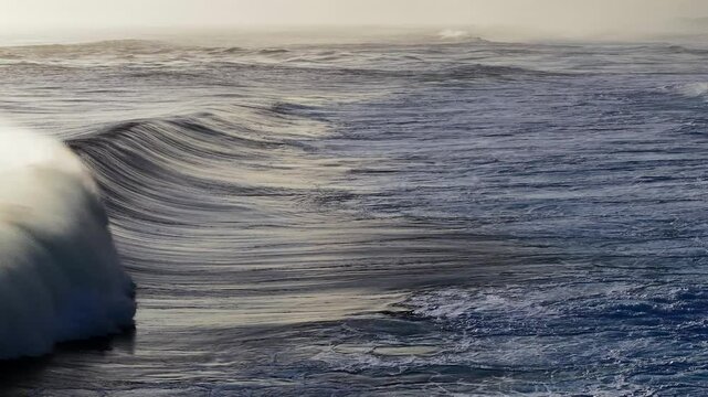 Aerial view of rolling waves crashing over a reef in slow motion. The surf creates a mesmerizing texture.