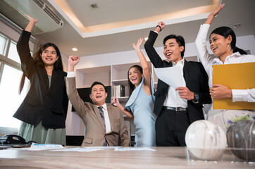 Happy business team celebrating successful achievement in office and raising hands with excitement and joy. Teamwork and motivation business concept