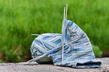 hellblau gemusterte Sockenwolle mit halb gestricktem Socken, Stricknadeln im Strickgut, liegen auf...