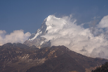 A breathtaking view of the snow-capped peak Machapuchare when the clouds softly hug the mountains in great Himalayas in Nepal.