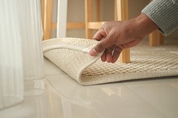 Person lifting edge of a woven rug indoors