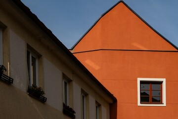 Bright orange modern house facade in sunlight, contrasted with a shaded beige building and blue sky. Contemporary architecture with geometric lines and bold colors
