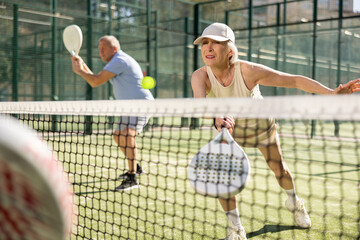 Determined sporty older woman doing her best playing padel in court