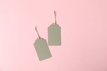 Blank tags with strings on pink background, flat lay