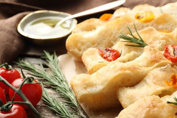 Cut delicious focaccia with tomatoes, rosemary and oil on table, closeup