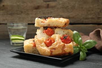 Pieces of delicious focaccia with tomatoes, basil and glass of water on gray table