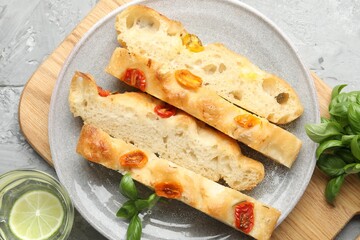 Pieces of delicious focaccia with tomatoes, basil and glass of water on gray textured table, flat lay