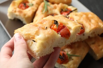Woman holding piece of delicious focaccia with tomatoes and spices at table, closeup