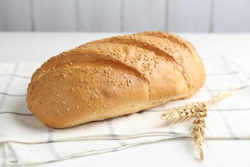 Fresh bread loaf and spikelets on white wooden table, closeup