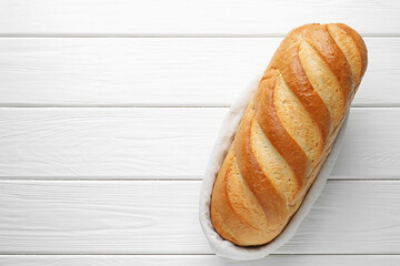 One bread loaf in basket on white wooden table, top view. Space for text