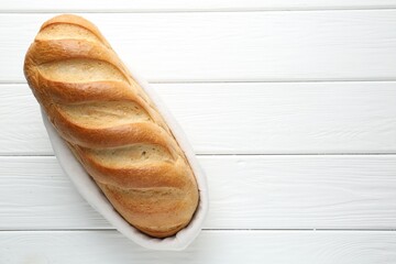 One bread loaf in basket on white wooden table, top view. Space for text