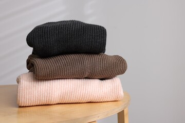 Stack of woolen sweaters on wooden table against light background. Space for text