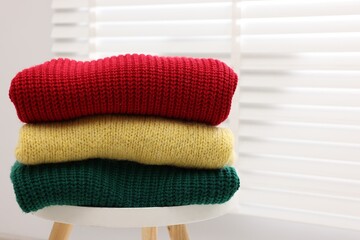 Stack of woolen sweaters on table near window, closeup