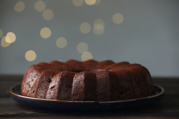 Tasty chocolate bundt cake on wooden table, closeup. Bokeh effect