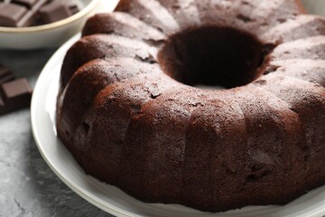 Tasty bundt cake and pieces of chocolate on grey table, closeup
