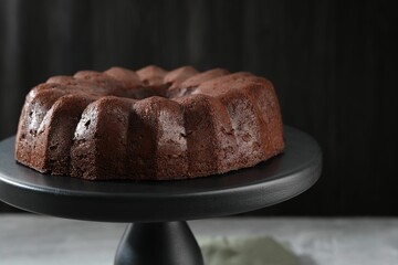Tasty chocolate bundt cake on stand against blurred background, closeup
