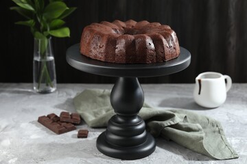 Tasty bundt cake, pieces of chocolate, sauce and green leaves on grey table, closeup