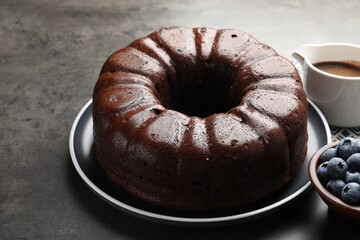 Tasty chocolate bundt cake and blueberries on grey table, closeup