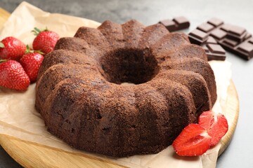 Tasty bundt cake, chocolate pieces and strawberries on grey table, closeup