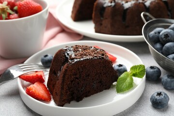 Piece of delicious chocolate bundt cake with strawberries, mint and blueberries on light grey textured table, closeup