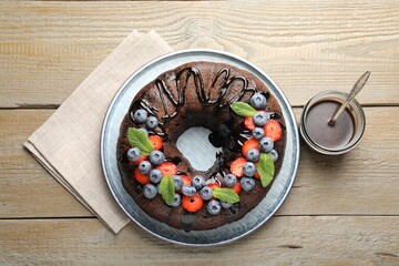 Delicious chocolate bundt cake with strawberries, mint and blueberries on wooden table, flat lay