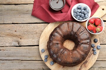 Delicious chocolate bundt cake, strawberries and blueberries on wooden table, flat lay. Space for...