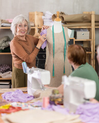 Sewing school senior woman teacher conducts lesson for elderly students, using mannequin to explain...