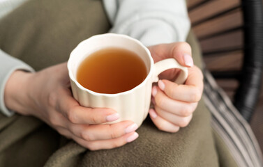 Woman holding a cup of hot tea while sitting cozy under a blanket, warming hands on a chilly day.