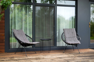 Two modern chairs and a small table on a wooden terrace by glass doors. Minimalistic outdoor seating area for relaxation.