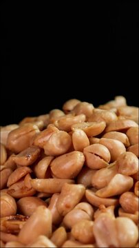 Slow motion close-up of roasted peanuts being peeled on a dark background. Suitable for advertising or promotion. Vertical shot
