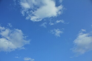 Obraz premium Clear blue sky with soft white cumulus clouds on a sunny day, providing a tranquil and natural background with green grass