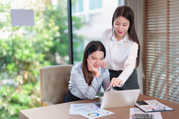 Two Young Asian Businesswomen Collaborate on Laptop in Office Meeting Analyzing Financial Reports