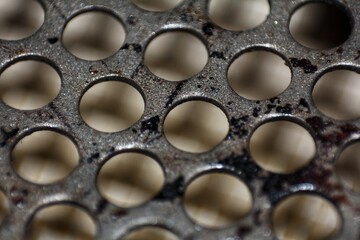 Detailed macro photograph of a perforated dark metal surface, creating an abstract industrial background with a repeating circular pattern