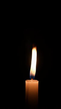 A candle burns in the dark, black background.